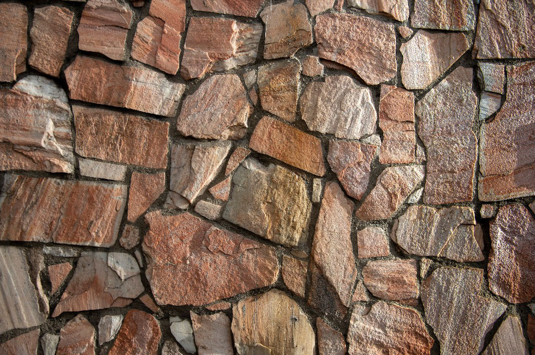 Unregelmäßig angeordnete rotbraune Natursteine mit sichtbarem grauem Fugenmörtel